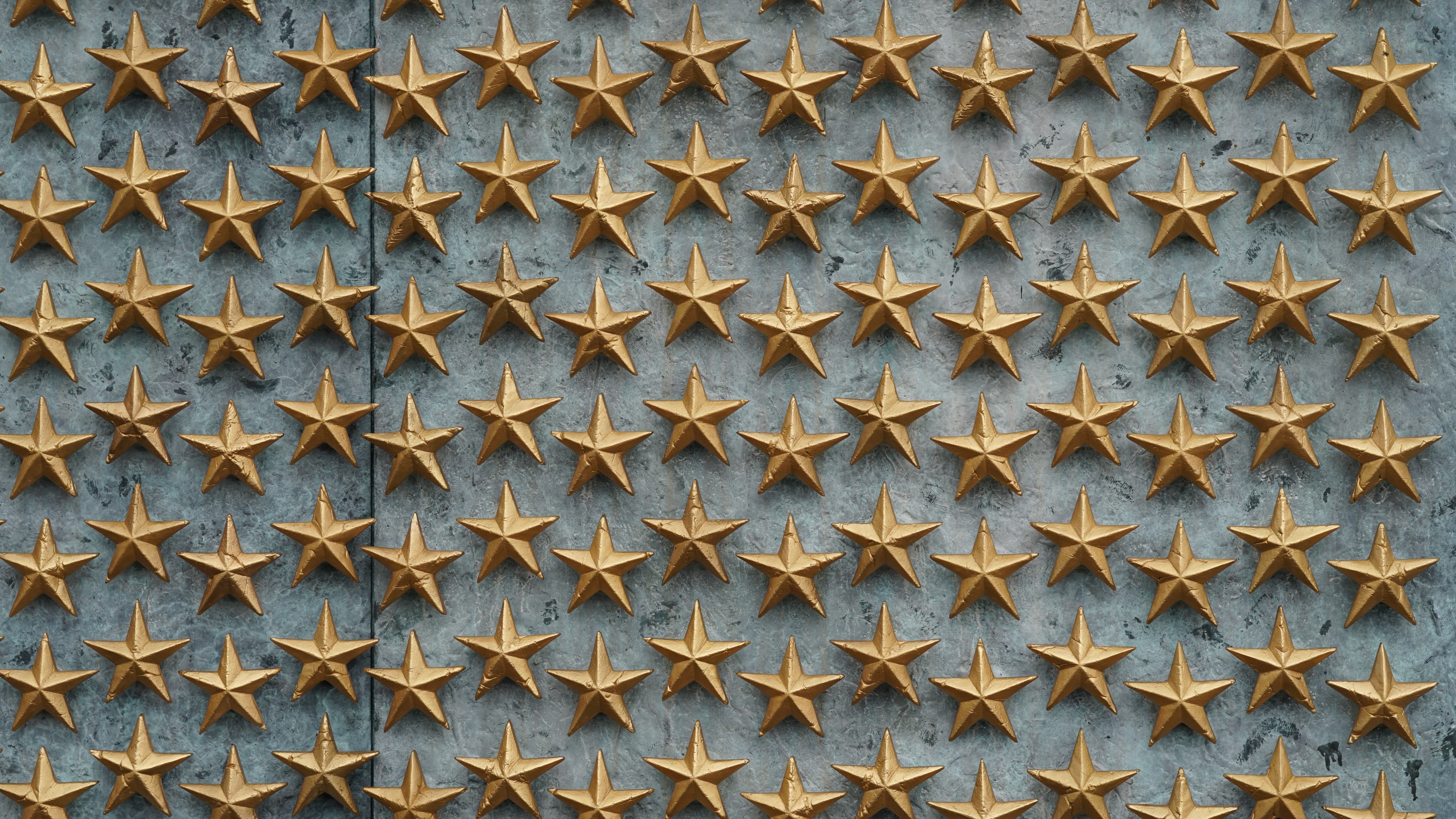 Rows of gold stars on a textured gray stone wall at the WWII Memorial.