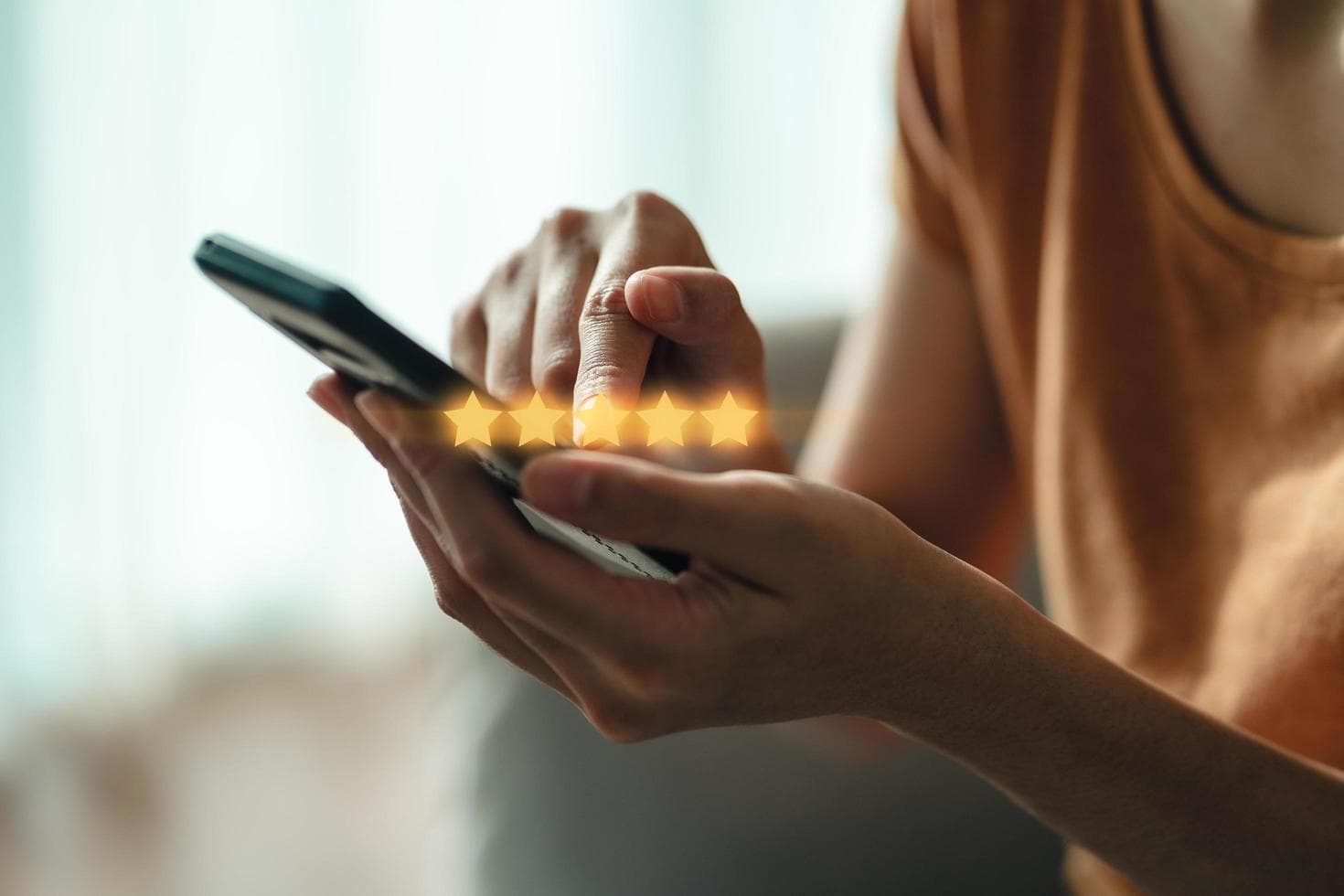 Person holding a smartphone and selecting a five-star rating with glowing yellow star icons.